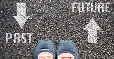 Asphalt background with the words "Past" and "Future" in white paint.  Toes of tennis shoes point toward Future.