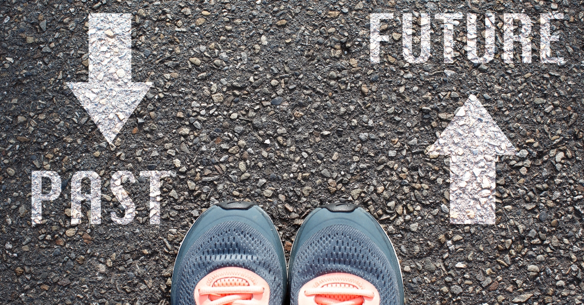 Asphalt background with the words "Past" and "Future" in white paint.  Toes of tennis shoes point toward Future.